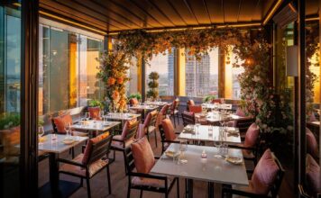 Rooftop dining terrace at sunset with tables set for dinner, pink cushions and floral installations