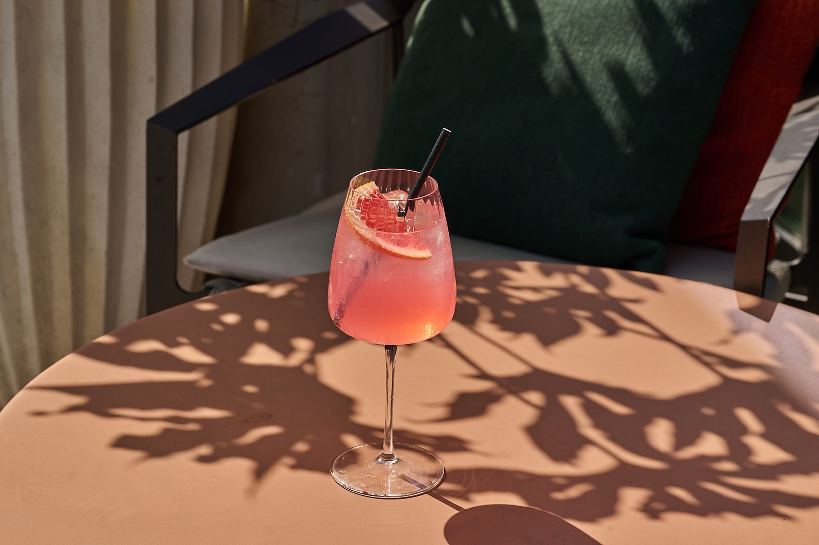 Pink cocktail garnished with grapefruit on a sunlit table