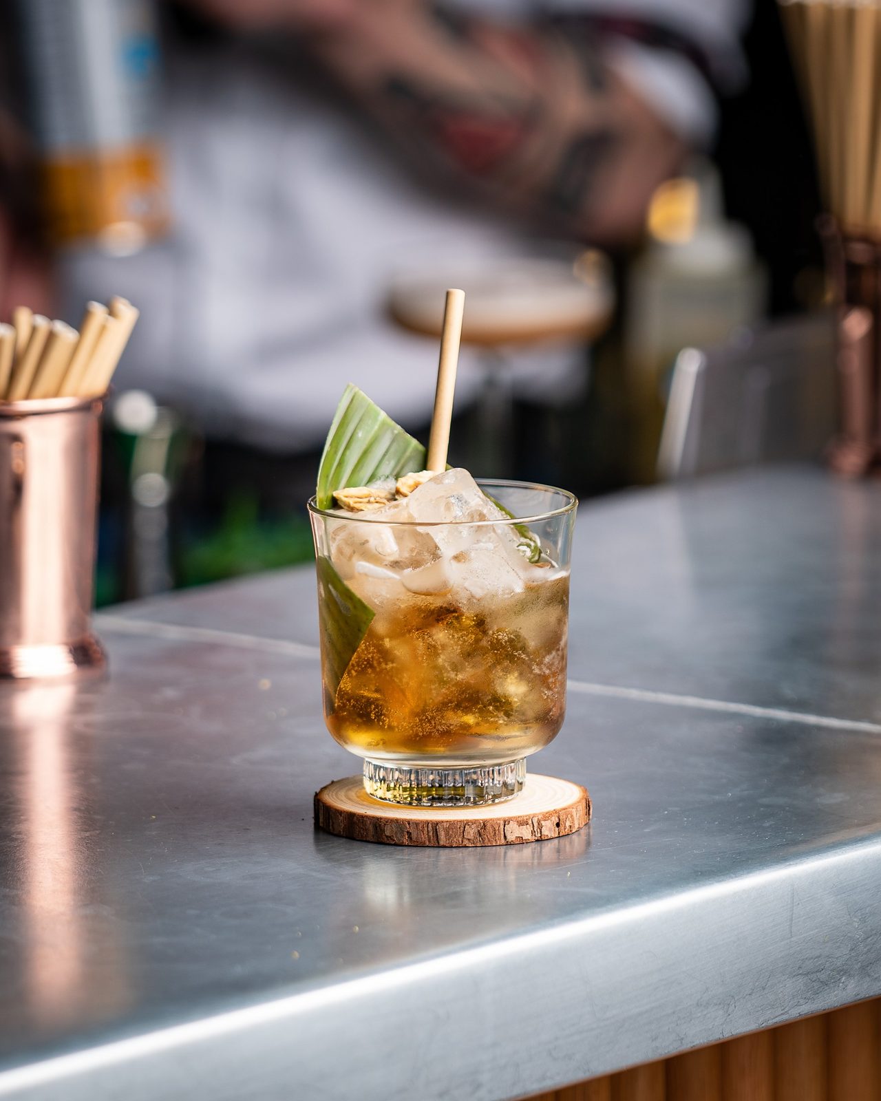 Amber cocktail with ice and a leaf garnish in a short glass on a bar counter