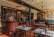 Bar with timber cabinetry and a curved counter beside marble-topped dining tables at Dishoom Borough