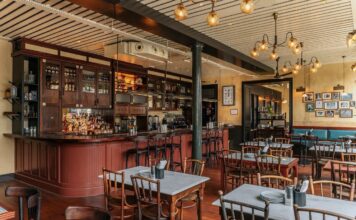 Bar with timber cabinetry and a curved counter beside marble-topped dining tables at Dishoom Borough