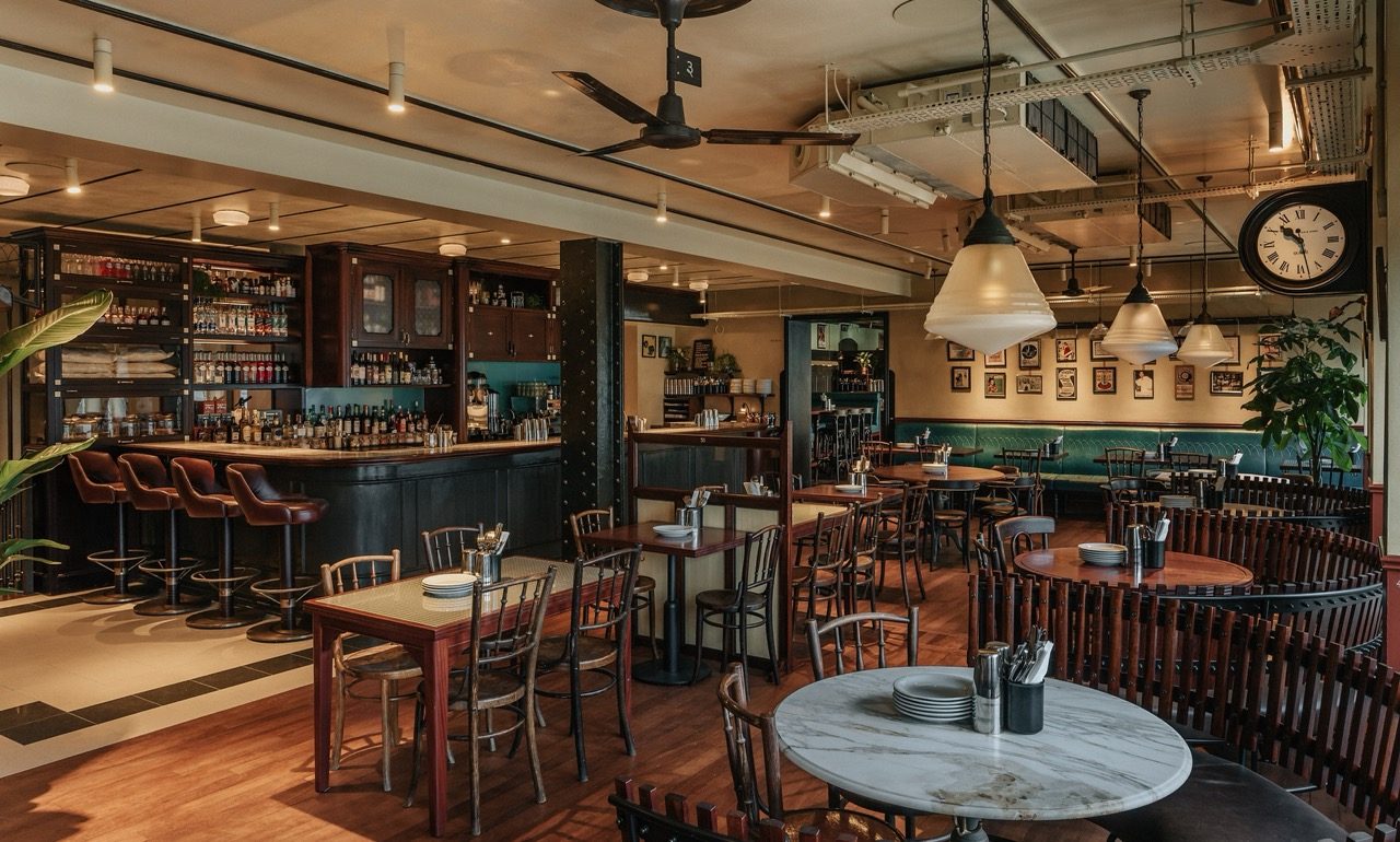 Bar and dining room with leather bar stools, bentwood chairs, pendant lights and a wall clock at Dishoom Borough