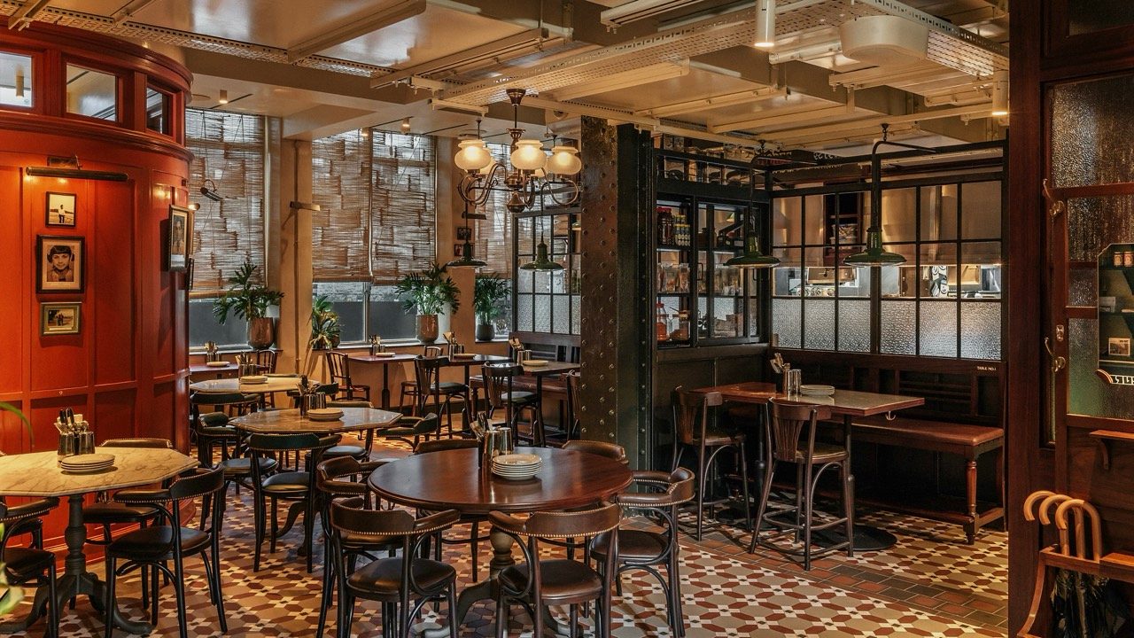 Dining room with patterned tile floor, red timber panelling, reed blinds and glazed cabinets at Dishoom Borough