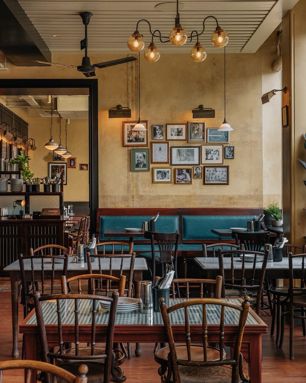 Dining area with marble-topped tables, a teal banquette and framed photographs on a distressed wall at Dishoom Borough