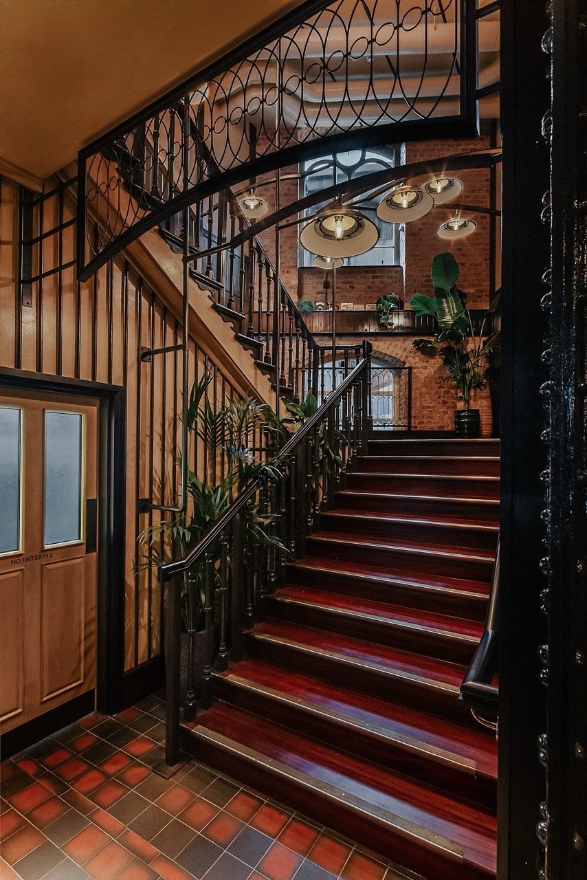 Staircase with ornamental timber treads, a metal balustrade and pendant lights at Dishoom Borough