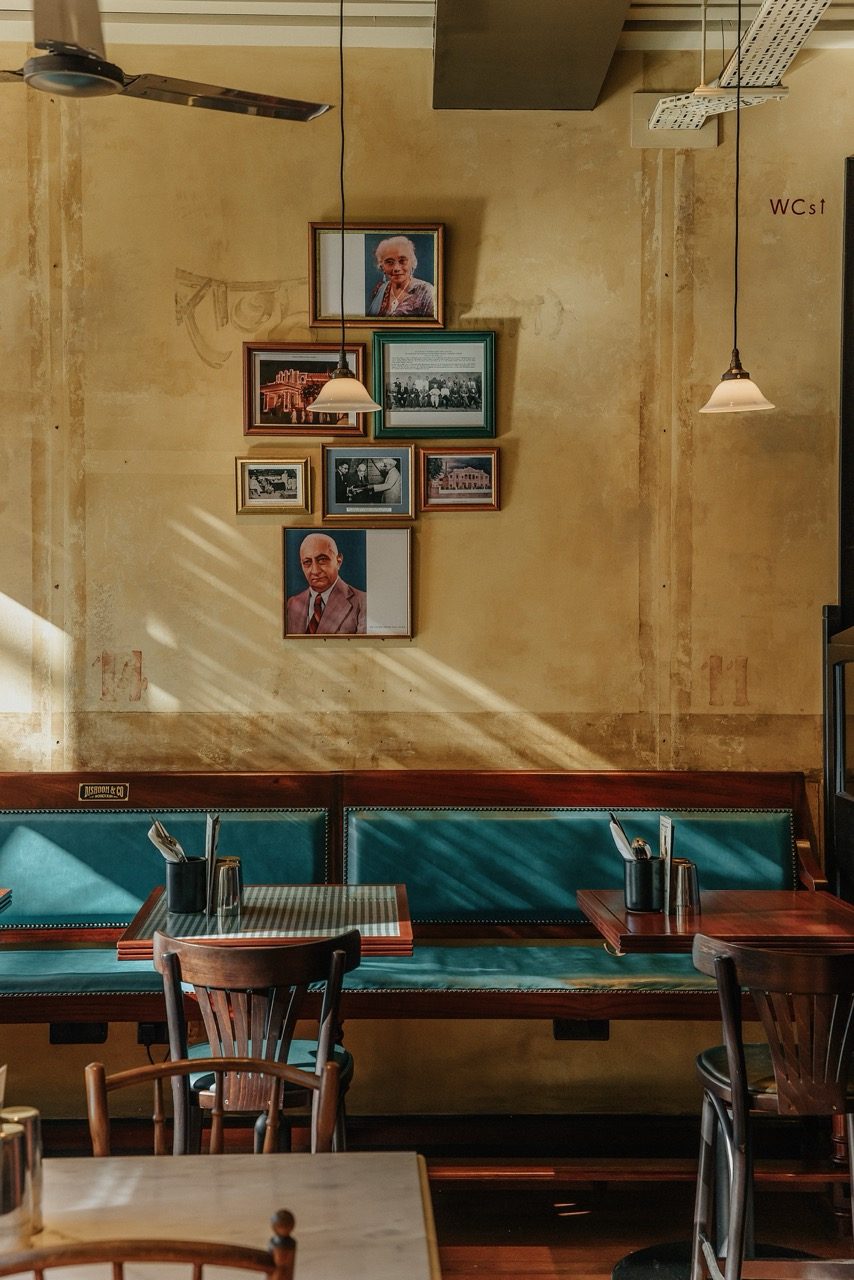 Teal banquette beneath framed portraits on a sunlit distressed wall at Dishoom Borough