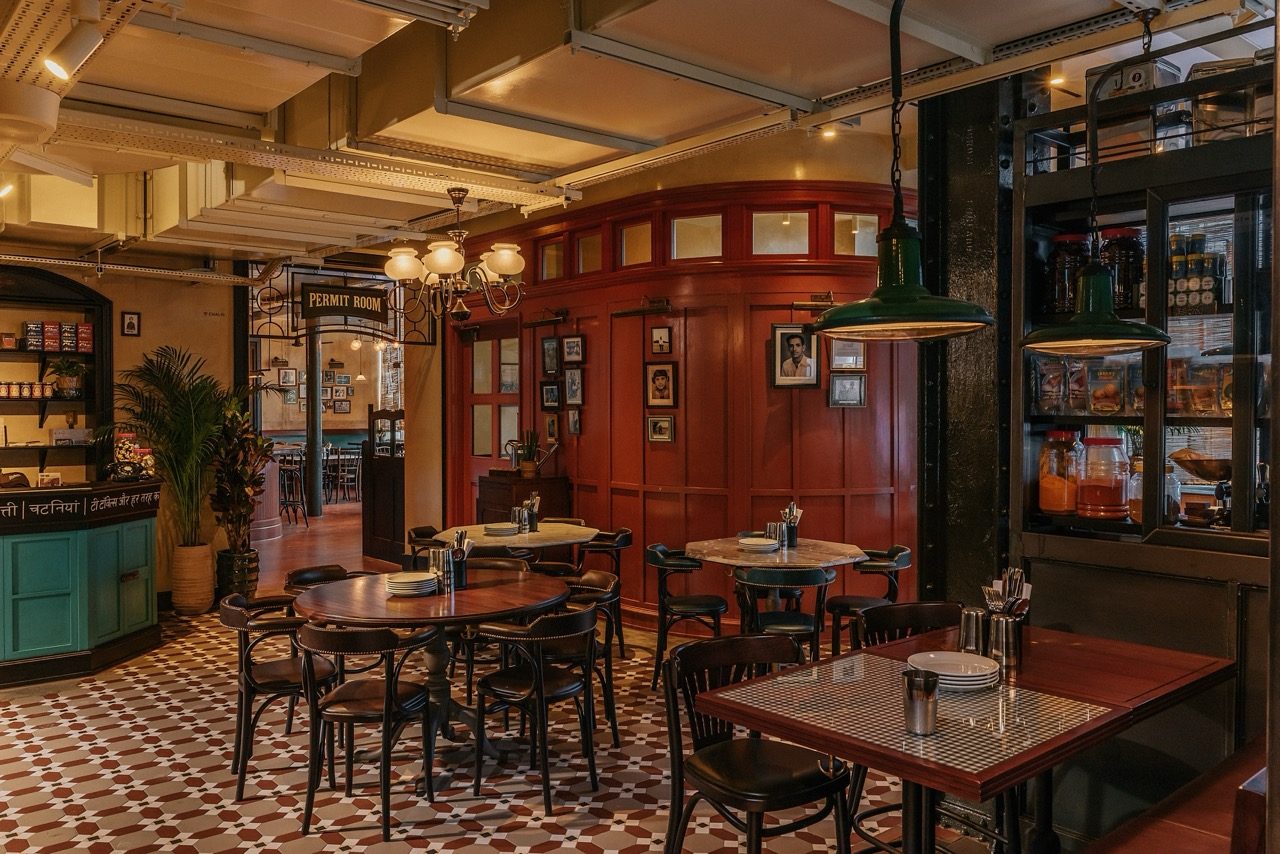 Dining area with a patterned tile floor, round tables and a Permit Room sign above a doorway at Dishoom Borough