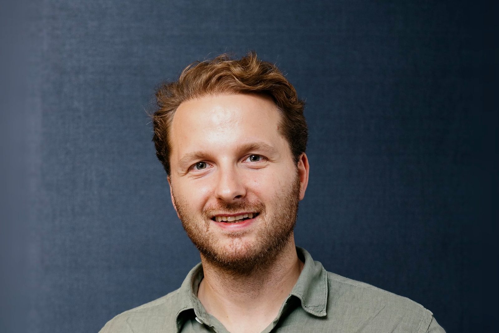 Jack Hurley, Commercial Director of Luxury Lodges, smiling in a green linen shirt against a dark blue backdrop