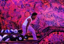 Bowler on a Lane7 lane in front of a pink and purple graffiti wall, with bowling balls on the return