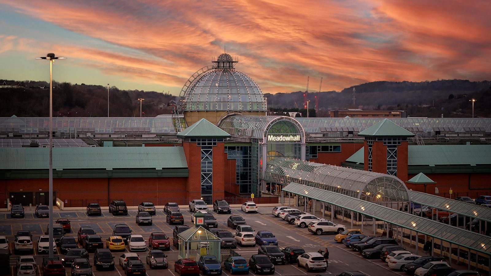 Meadowhall shopping centre entrance and glass dome at sunset, with the car park in front