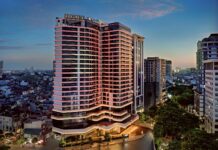 LÈGACY Hanoi – A Fusion Original tower at dusk, with the Hanoi cityscape around it