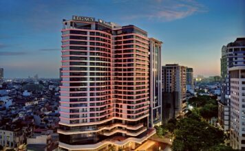 LÈGACY Hanoi – A Fusion Original tower at dusk, with the Hanoi cityscape around it