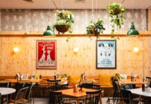 Dining room of a Rudy’s Pizza Napoletana pizzeria with wooden panelling, plants and framed posters