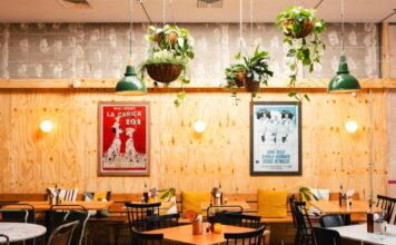 Dining room of a Rudy’s Pizza Napoletana pizzeria with wooden panelling, plants and framed posters