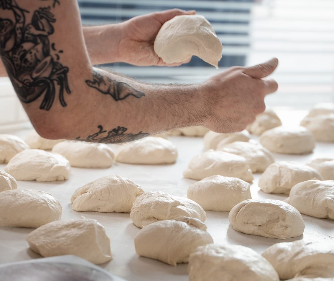 Pizza dough being shaped into balls on a floured work surface at Rudy’s