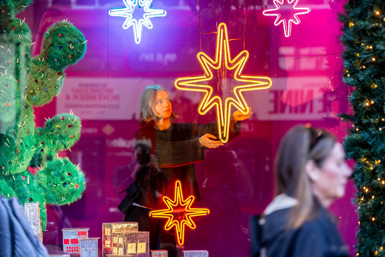 A neon star being hung in a Selfridges window display beside a jewelled green cactus