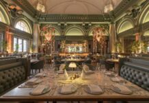 Tables set with glassware and lamps in tender’s dining room at the Stock Exchange Hotel in Manchester, with green arched walls, ornate plasterwork and an open kitchen at the far end