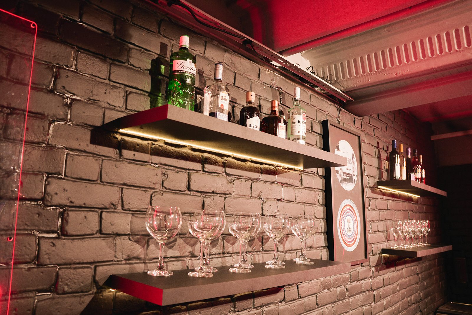 Spirits bottles and coupe glasses on lit shelves against a brick wall at UMusic Shop Camden