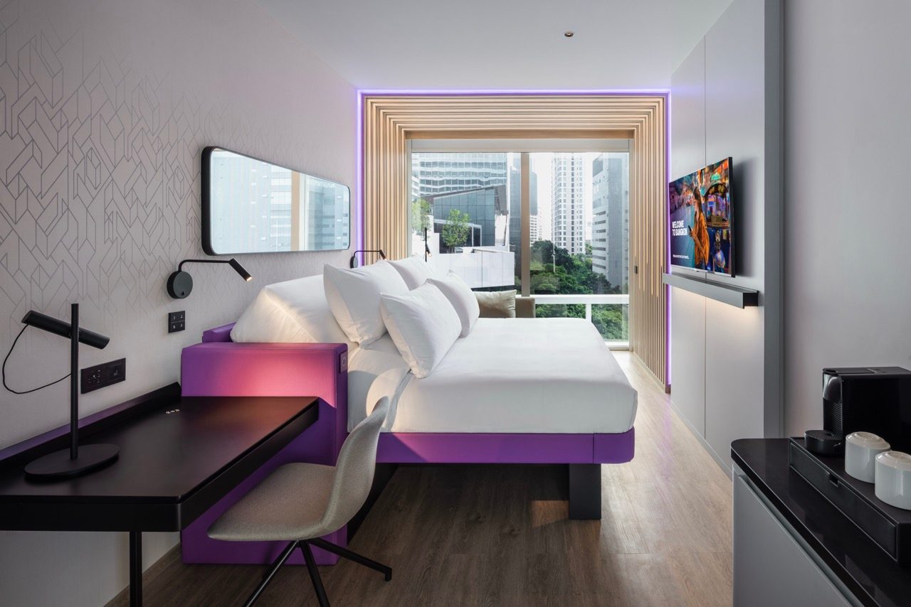 Guest room with a purple-framed bed, desk, wall-mounted TV and floor-to-ceiling window at YOTEL Bangkok Sukhumvit