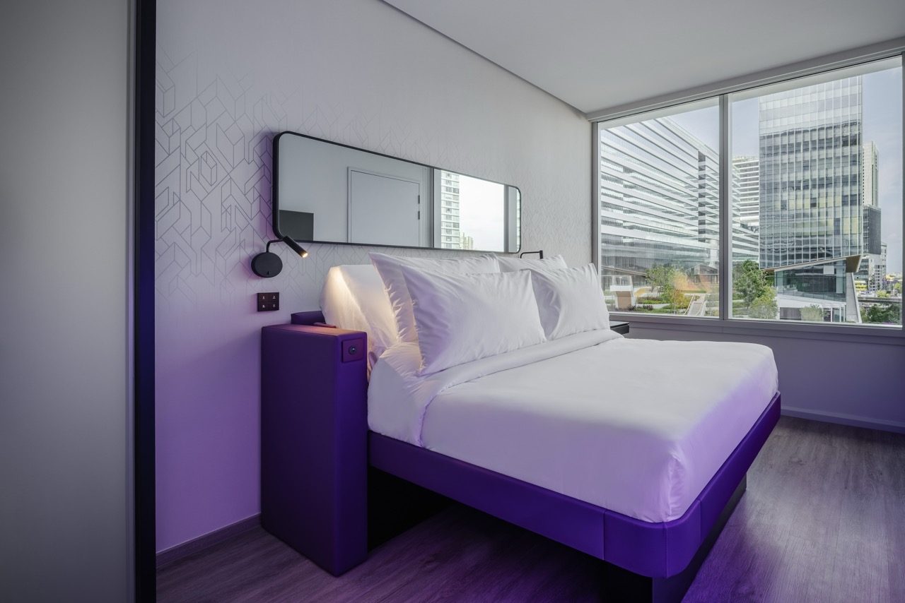 Guest room with a purple-framed bed and a window overlooking neighbouring towers at YOTEL Bangkok Sukhumvit