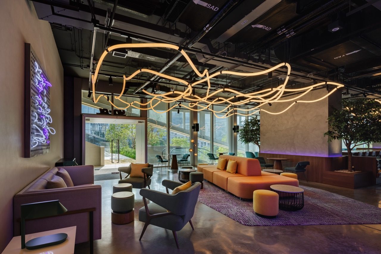 Lounge with a sculptural light installation, neon wall art, orange sofas and armchairs at YOTEL Bangkok Sukhumvit