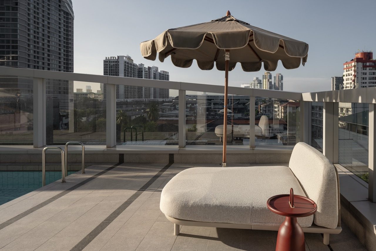 Poolside daybed with a parasol and side table overlooking the city at YOTEL Bangkok Sukhumvit