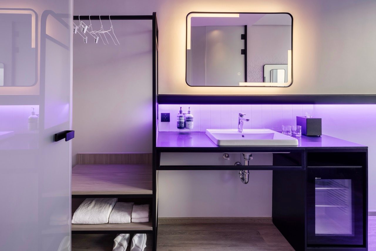 Vanity with a backlit mirror, basin, purple lighting and open wardrobe shelving at YOTEL Bangkok Sukhumvit