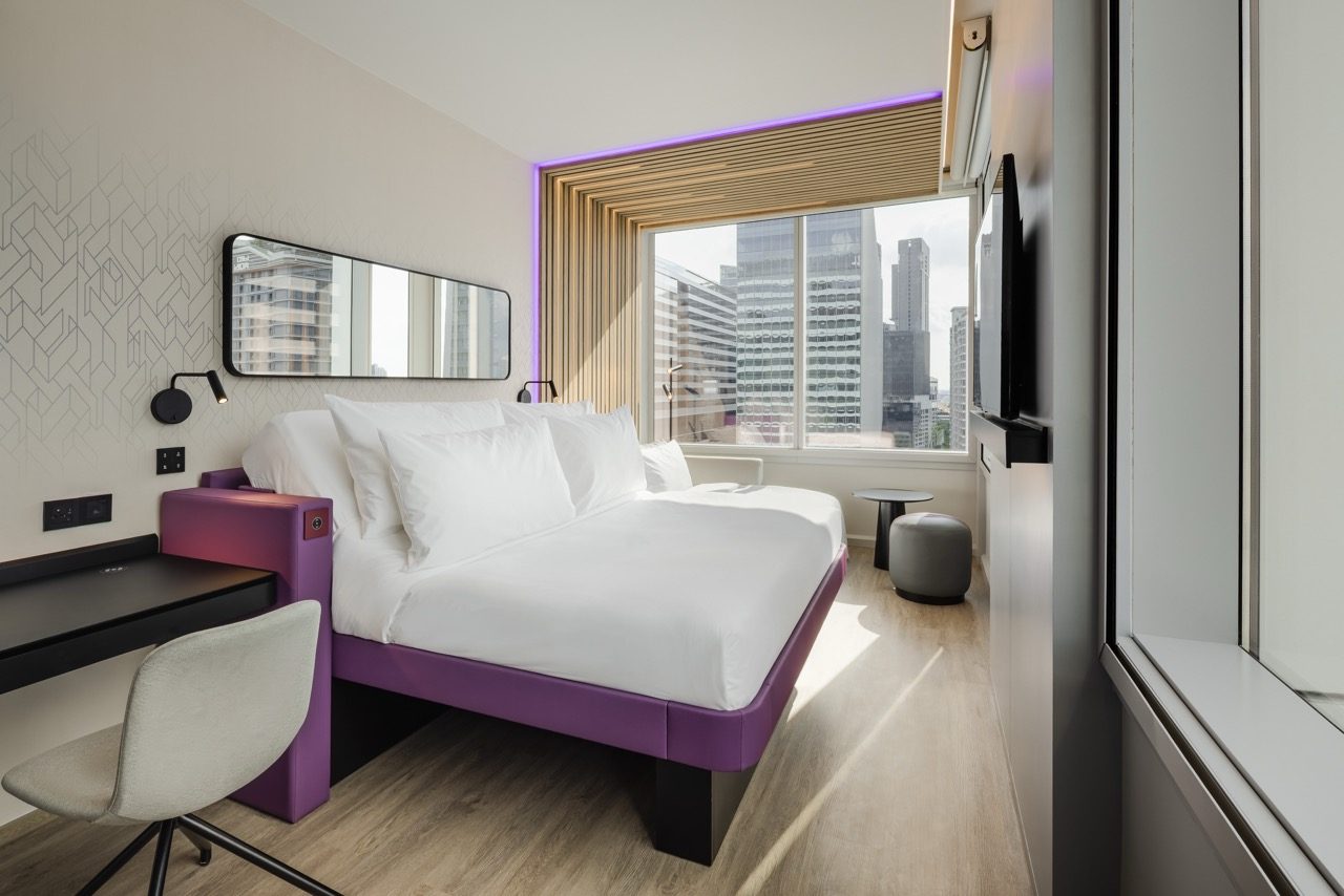 Guest room with a purple-framed bed, desk and window views of city towers at YOTEL Bangkok Sukhumvit